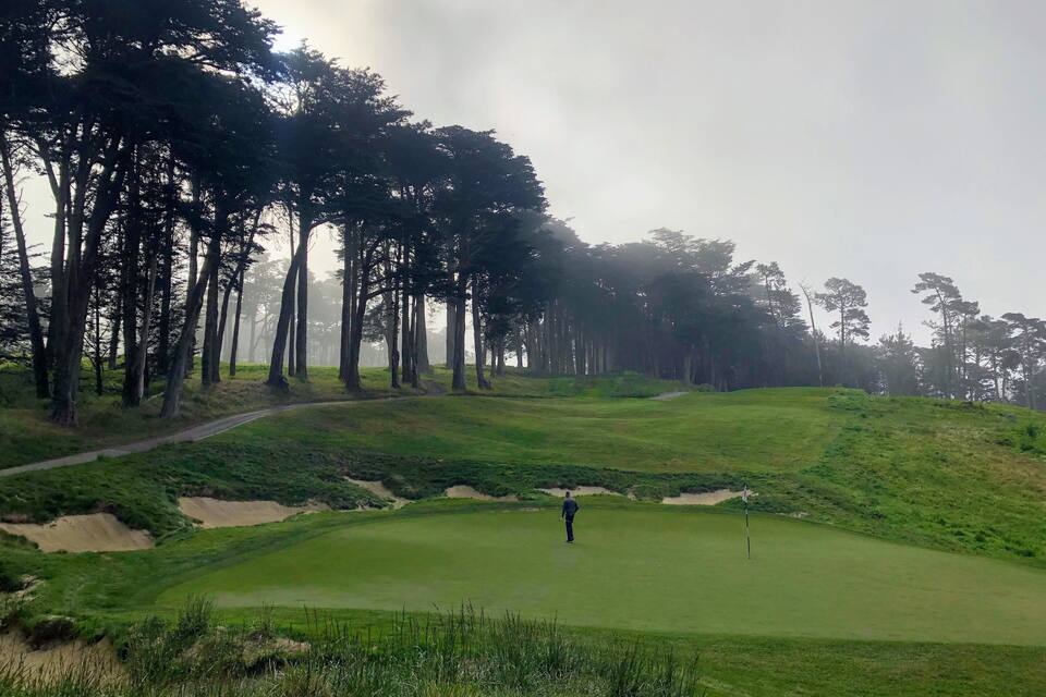 A golf course with sand bunkers, a flagstick, and tall trees.