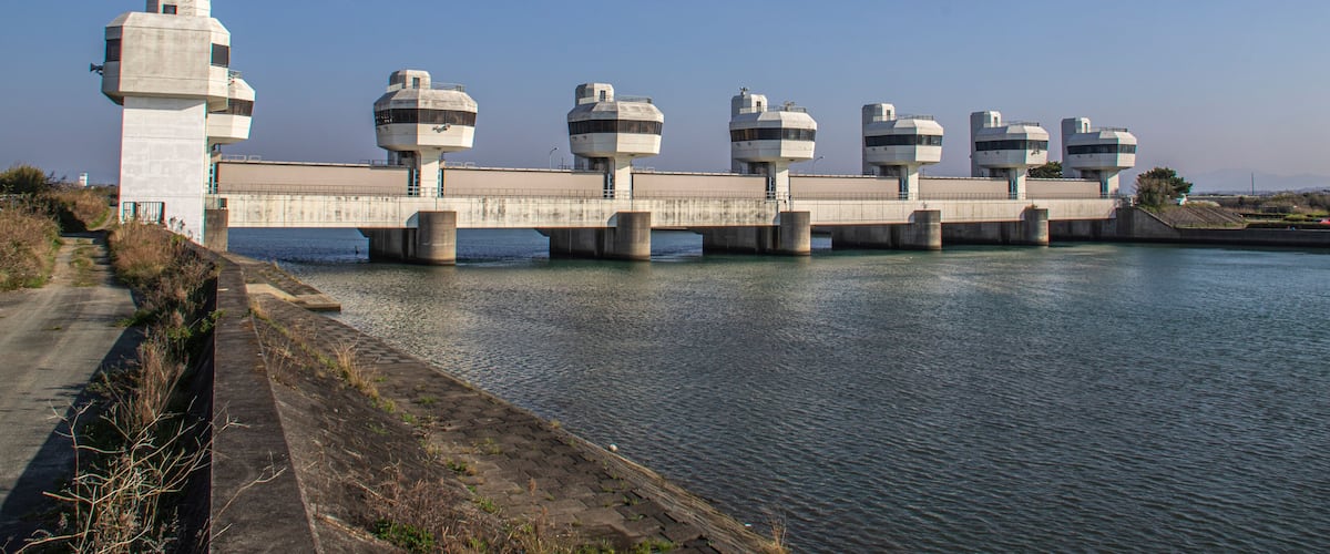 Eine Betonbrücke mit mehreren zylindrischen Bauwerken, die sich über ein Gewässer erstreckt.