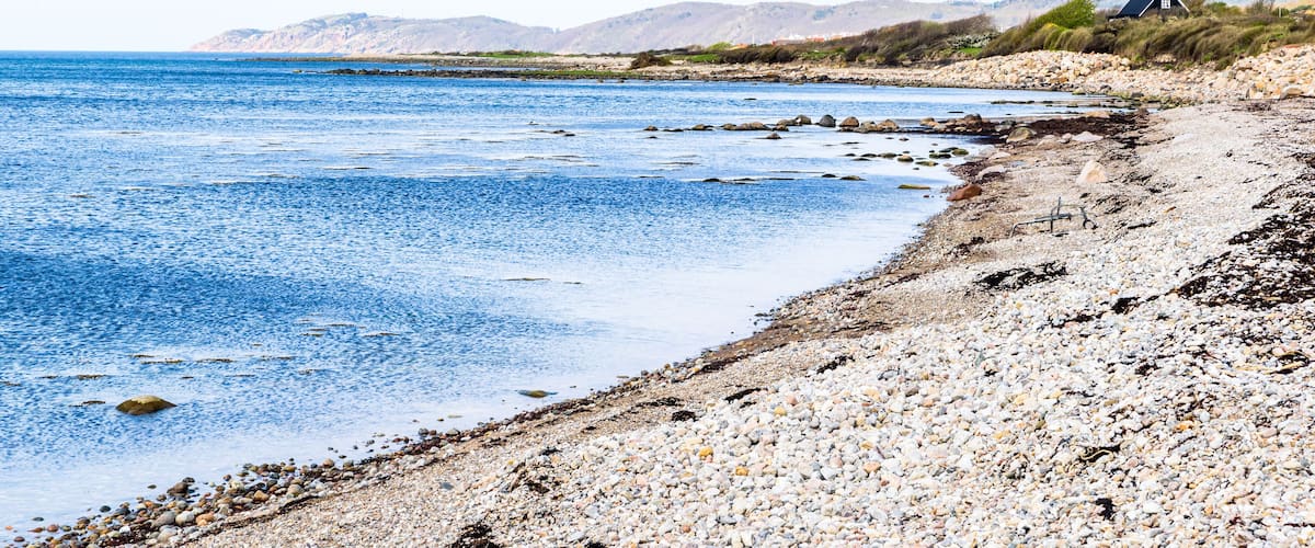 A pebble beach with a house on a hill.