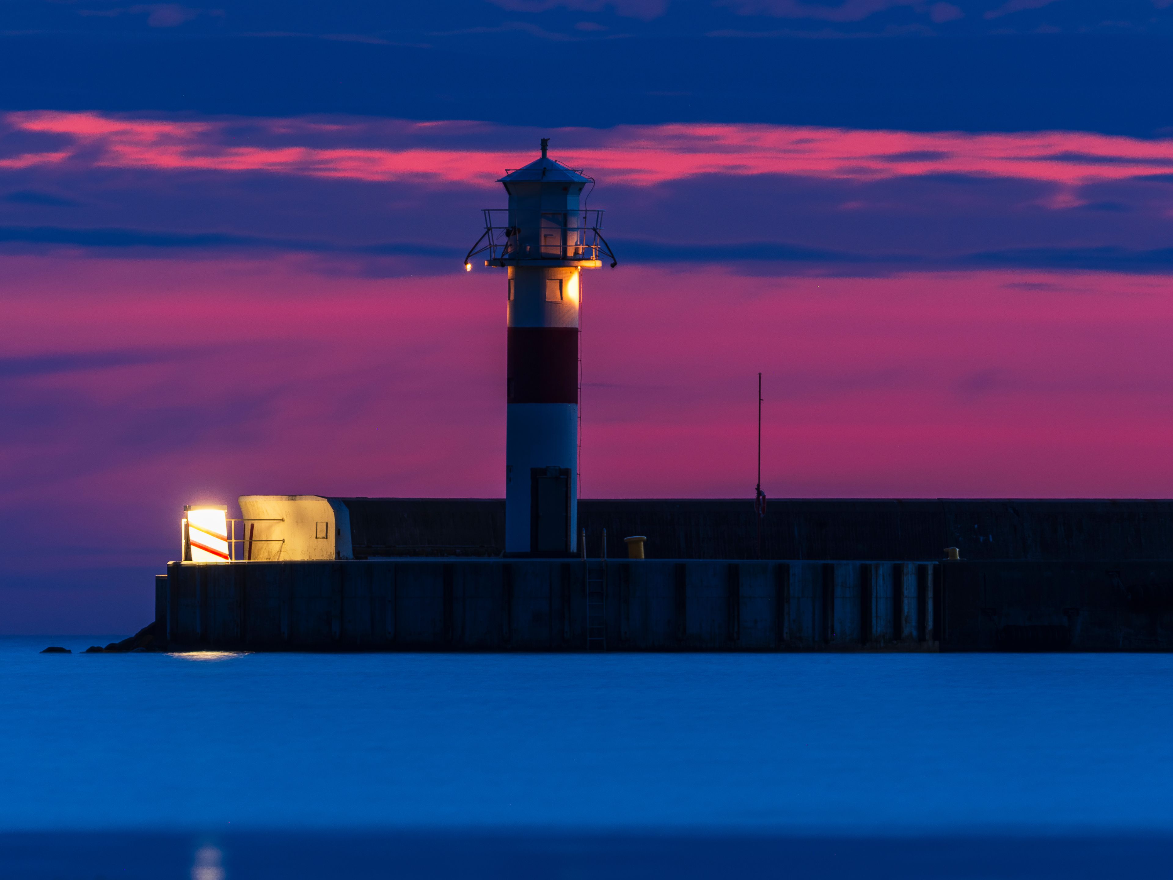 Stunning sunset over the lighthouse in Höganäs, Sweden highlighting the calm sea and vibrant sky hues