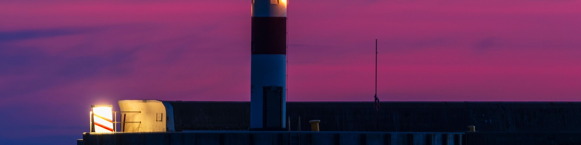 Un faro al atardecer bajo un cielo rosado y morado.