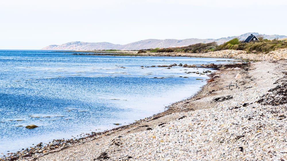 A pebble beach with a house on a hill.