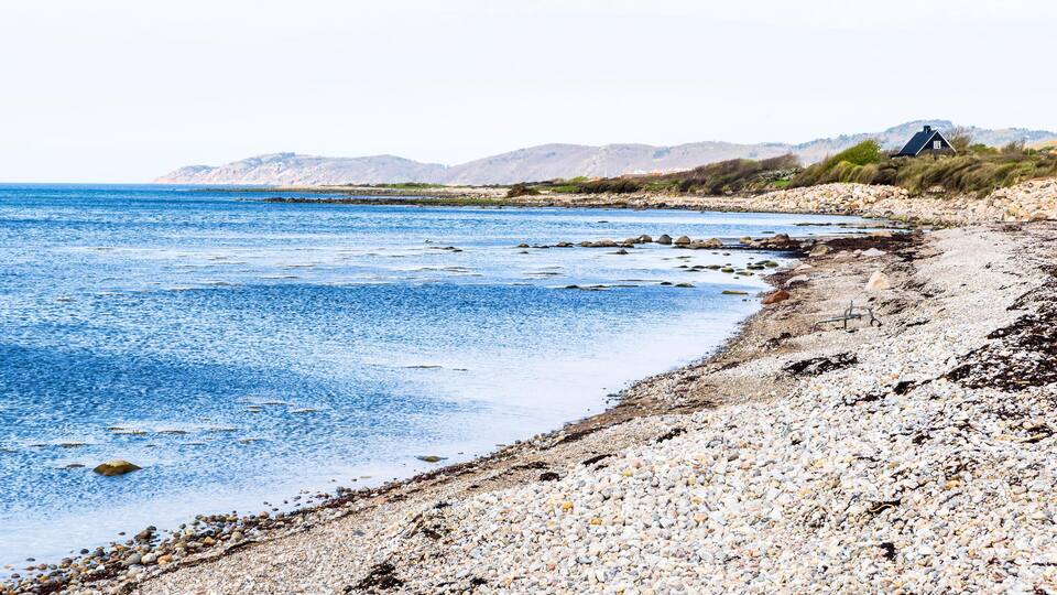 A pebble beach with a house on a hill.