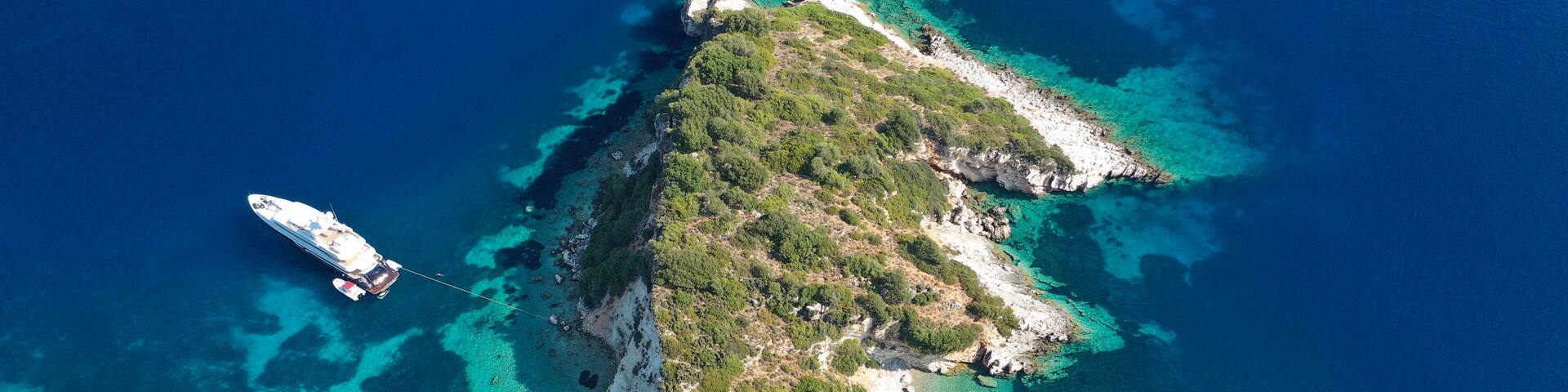An aerial view of a coastal island with clear turquoise waters, a sandy beach, and lush greenery.