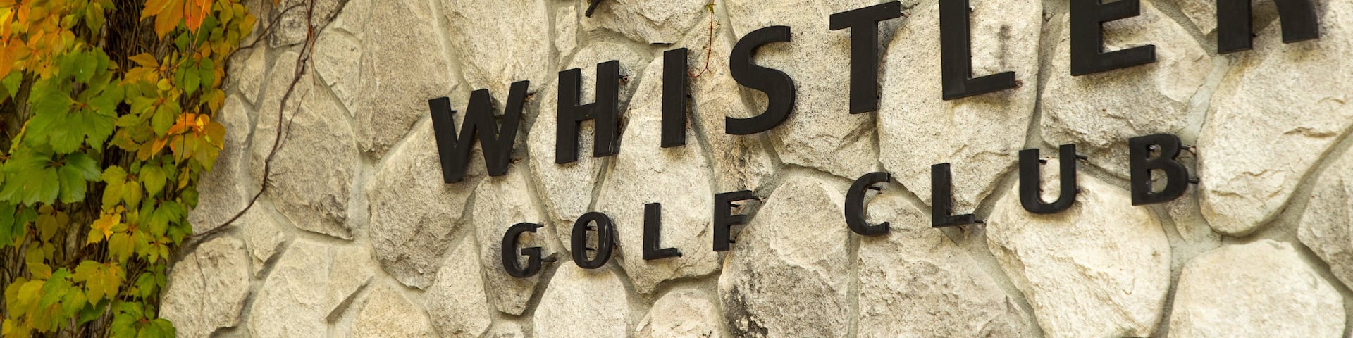A stone wall with the text "WHISTLER GOLF CLUB" and a logo above it.