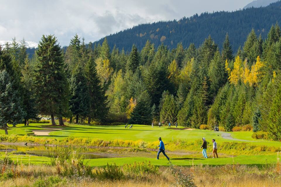 A golf course with lush greenery, a pond, and a forested mountain backdrop.