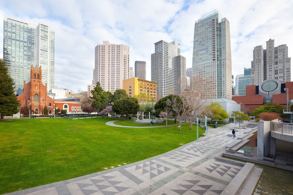 Un paisaje urbano con un parque verde extenso, edificios históricos y rascacielos modernos.