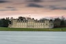 Een groot, statig gebouw met klassieke architectuur, een verzorgd gazon en een rustig waterpartij op de voorgrond.