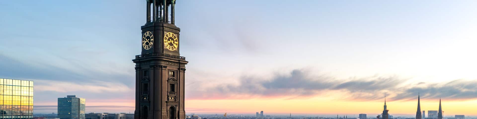 A cityscape with a prominent clock tower and a modern glass building.