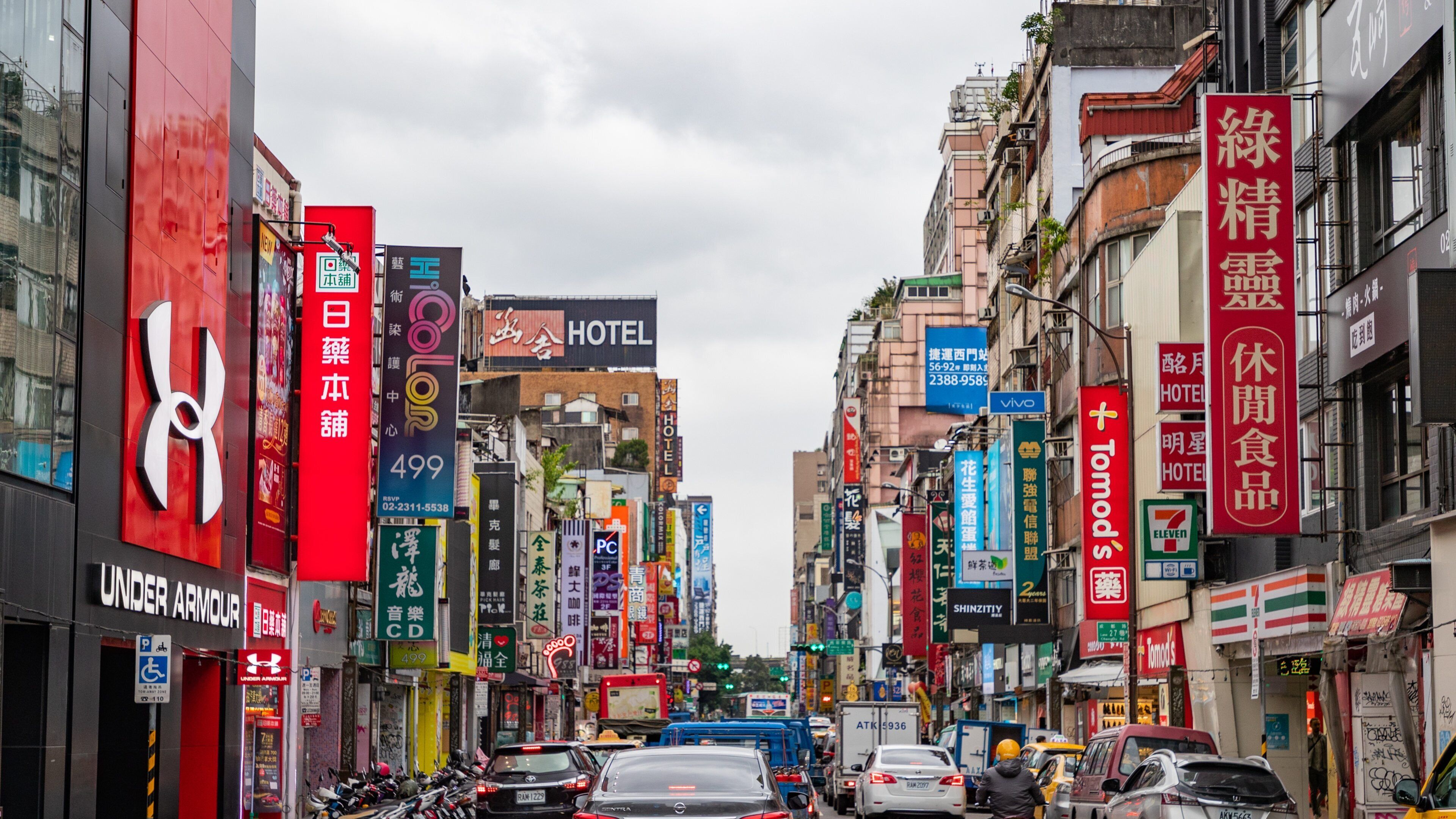 A busy urban street with various shops, signs, and vehicles.