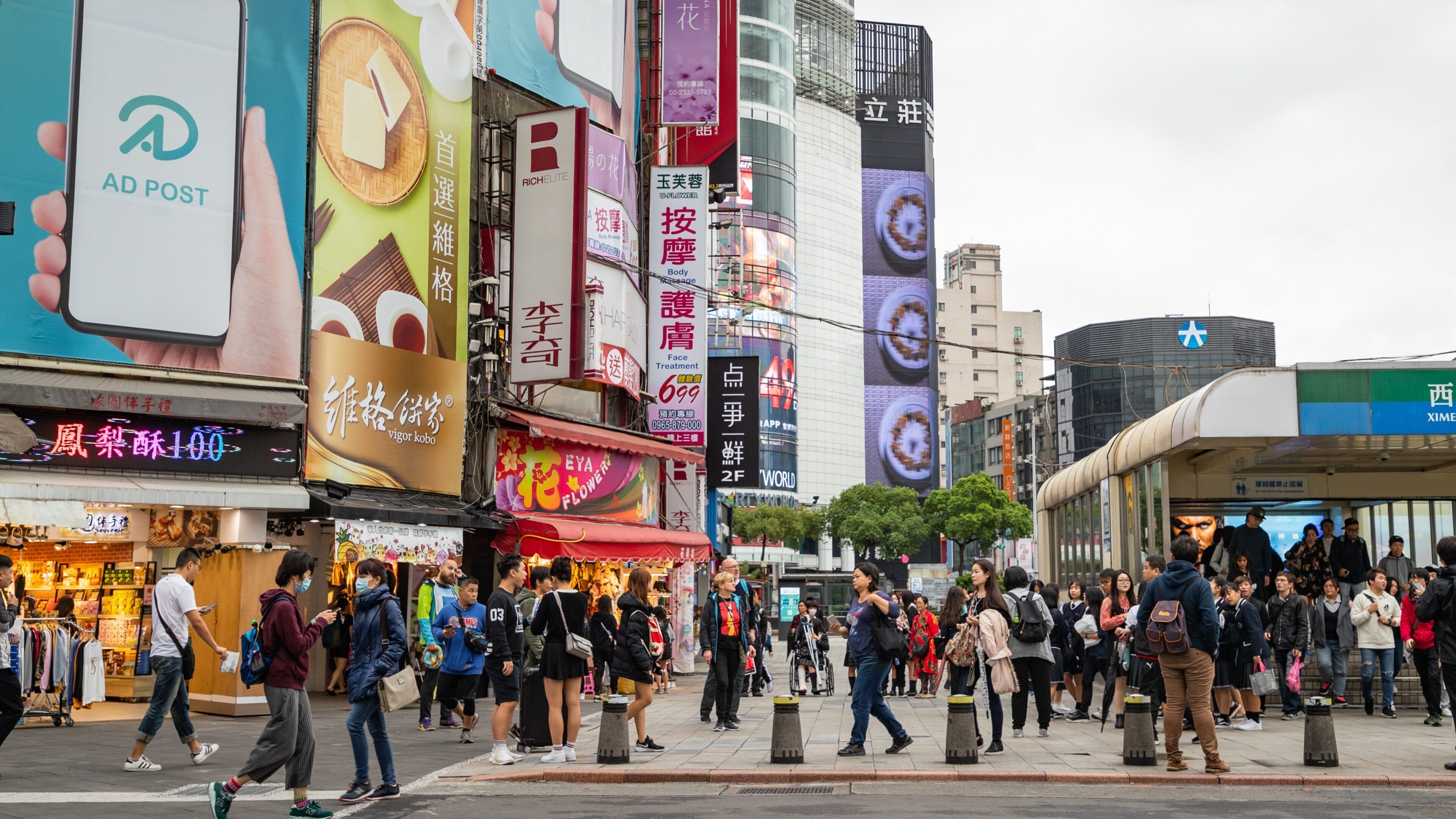 A busy urban street with tall buildings, billboards, and pedestrians.