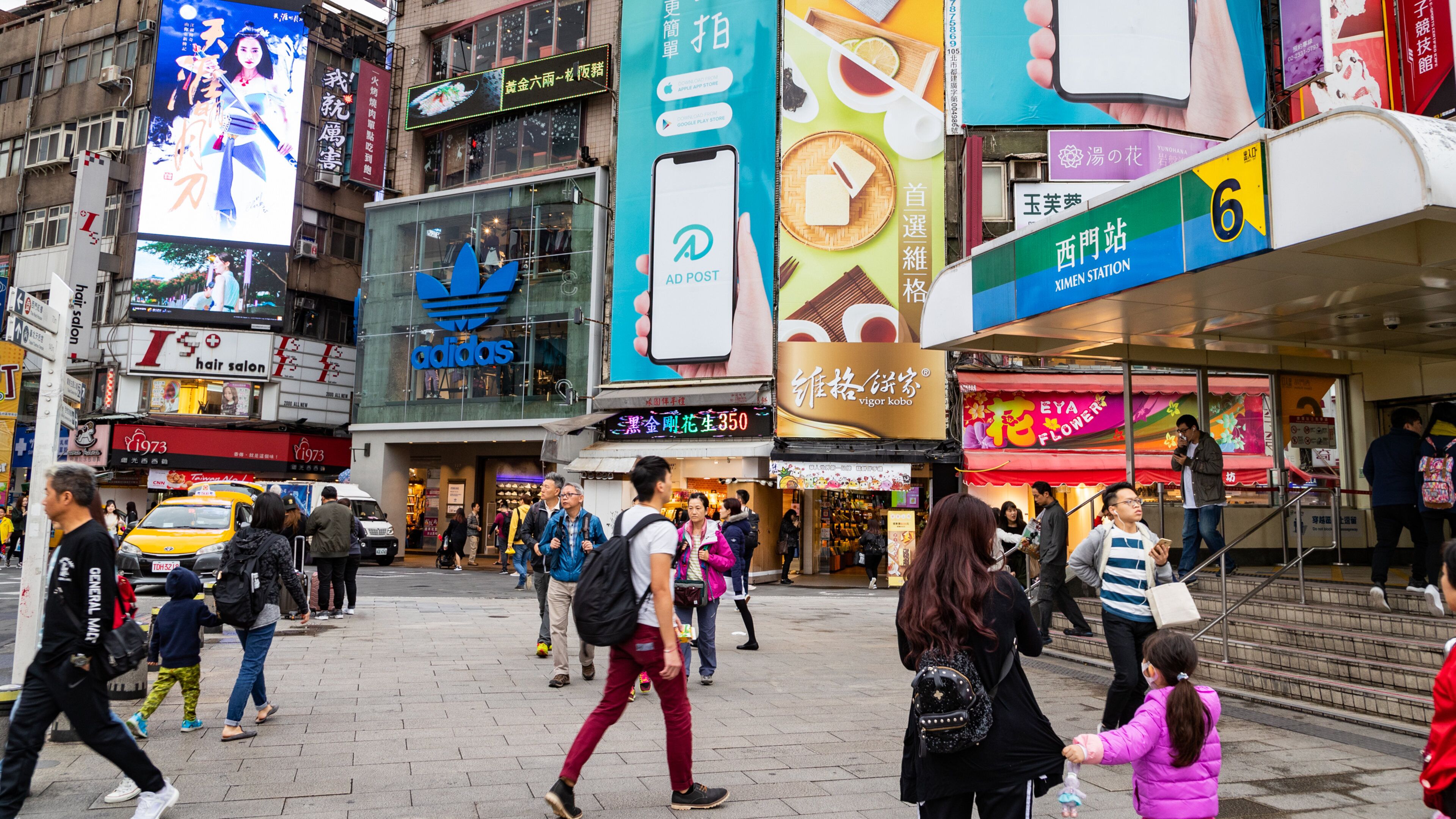 A busy urban street with pedestrians, storefronts, and advertisements.