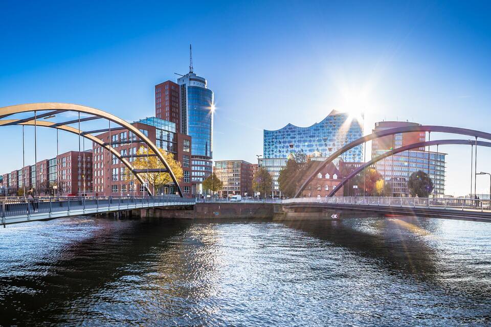Et moderne bybillede med en markant bro over en flod, der viser moderne arkitektur og en klar, blå himmel.