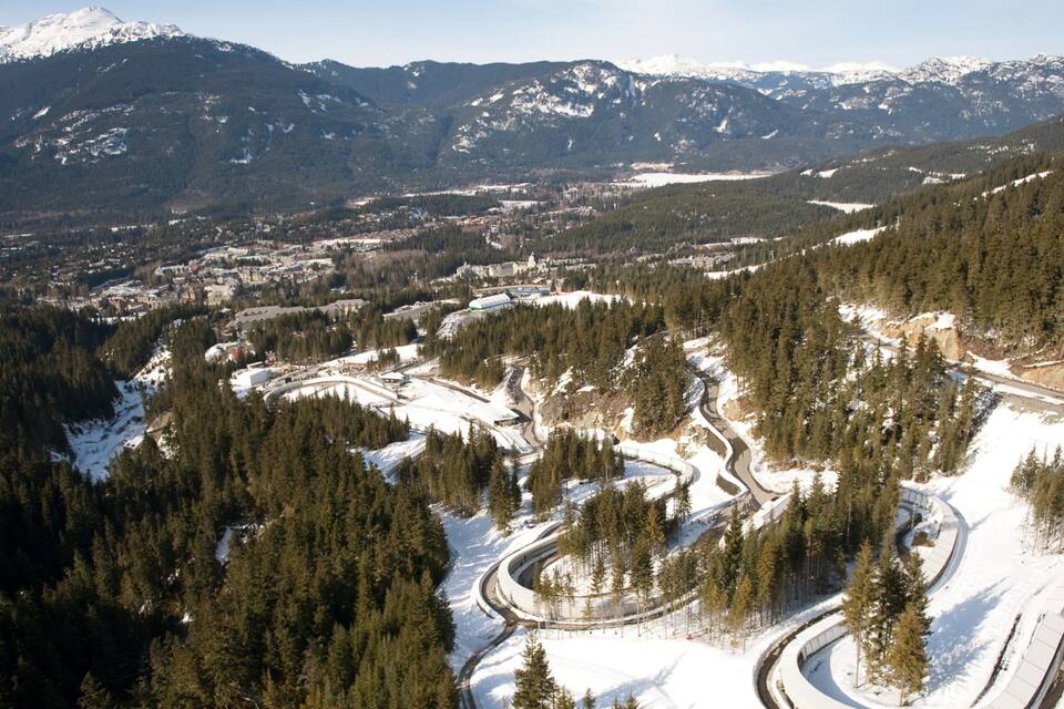A snow-covered mountain landscape with a winding road and dense forests.