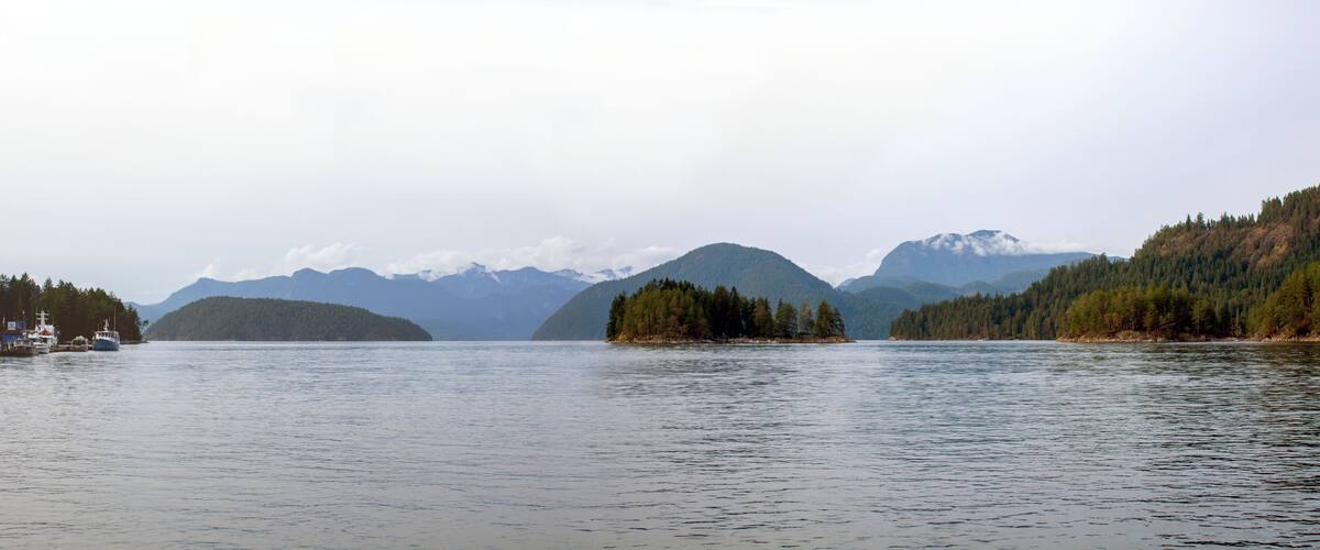A calm lake with boats, surrounded by forested hills and distant mountains.