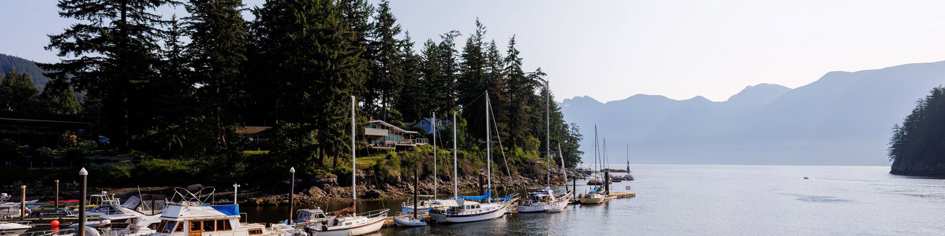 Boats at dock at the mouth of Snug Cove, Bowen Island looking to Howe Sound and Coast Mountains in the morning sun