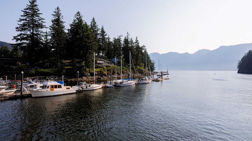 Boats at dock at the mouth of Snug Cove, Bowen Island looking to Howe Sound and Coast Mountains in the morning sun