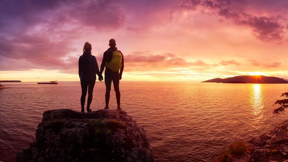 A sunset over a body of water with rocky shores and a forested coastline.