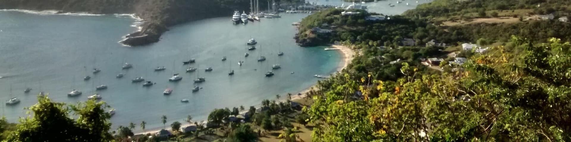 A coastal landscape with a bay filled with boats, surrounded by hills and dense greenery.
