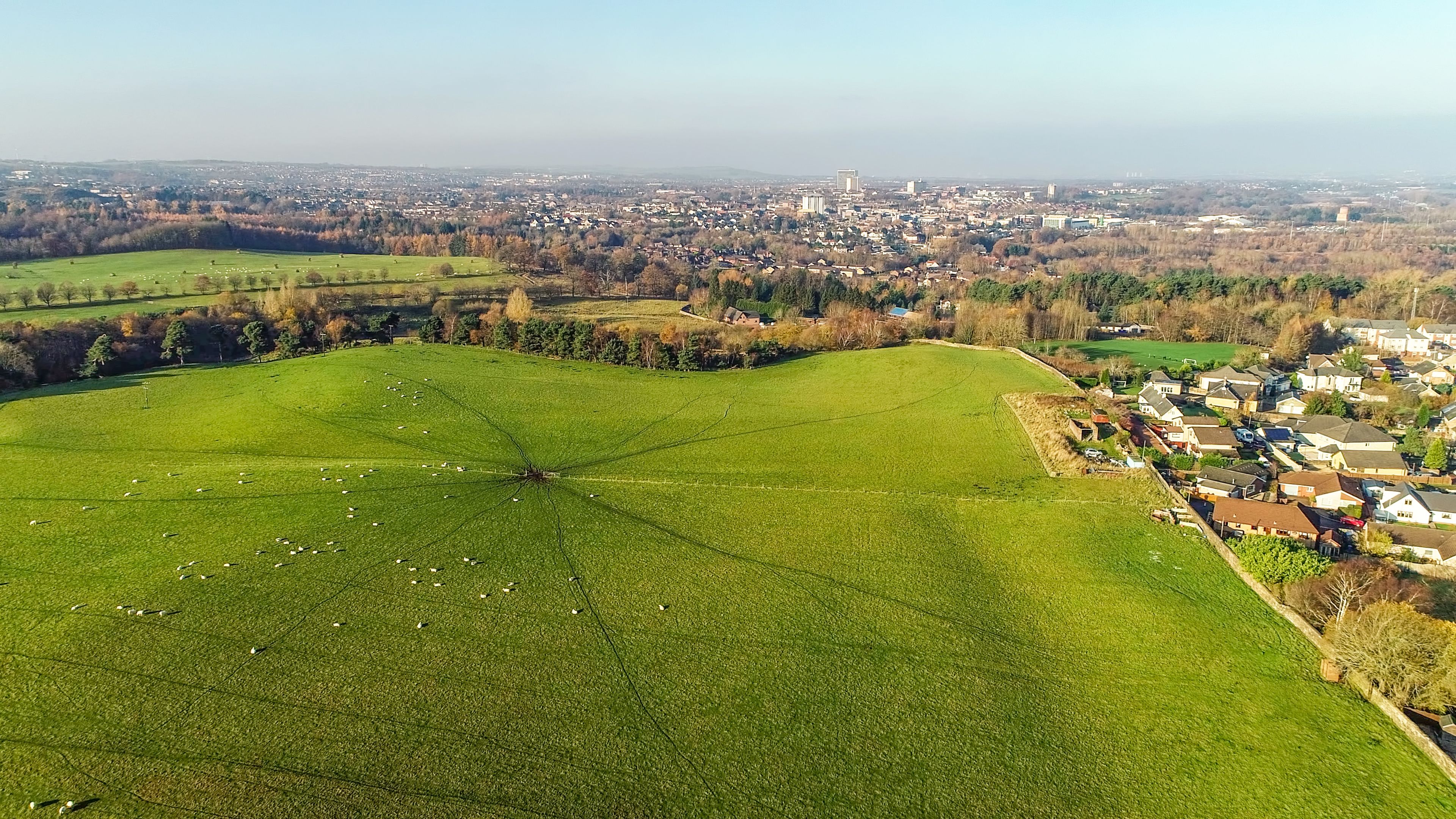 A green field with scattered sheep, a small village, and a distant cityscape.