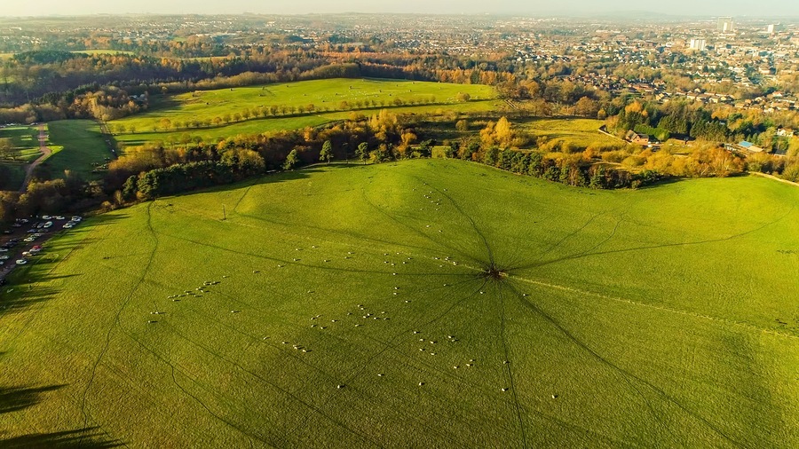 Un campo verde con una cerca, una carretera y un pueblo al fondo.