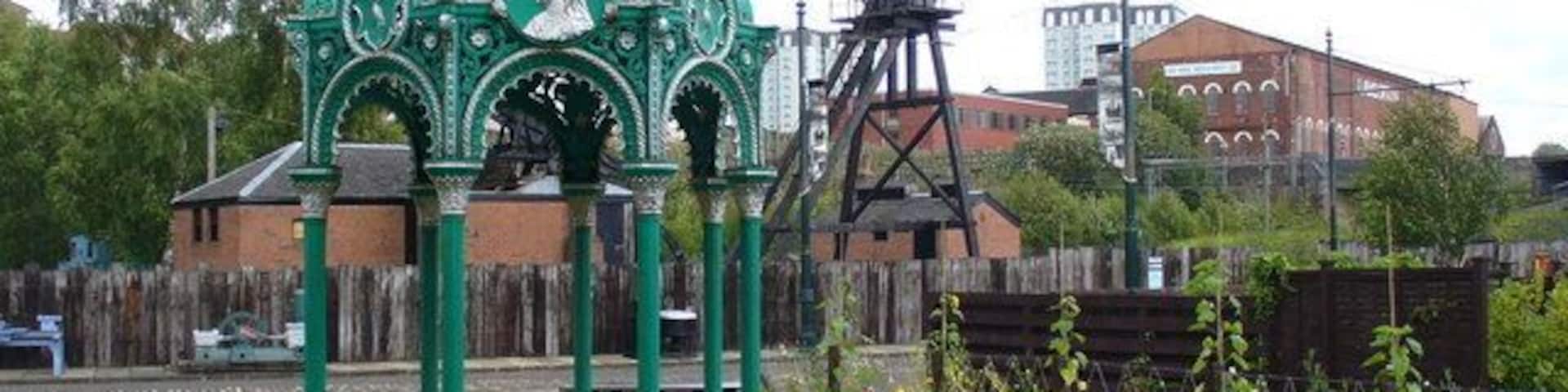 A gazebo with a green dome and intricate designs, surrounded by a grassy area with picnic tables.
