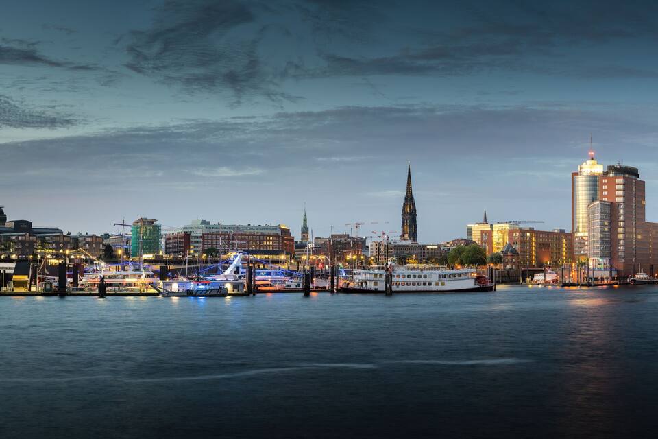 Byens skyline med et markant tårn og en flod med både.