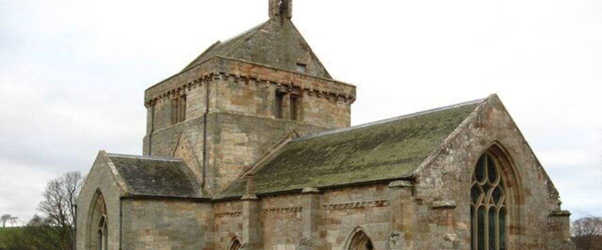 A historic stone church with a bell tower and a cemetery in front.