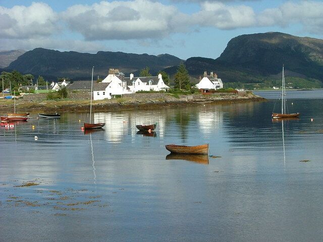 A calm lake with several boats, white houses, and mountains in the background.