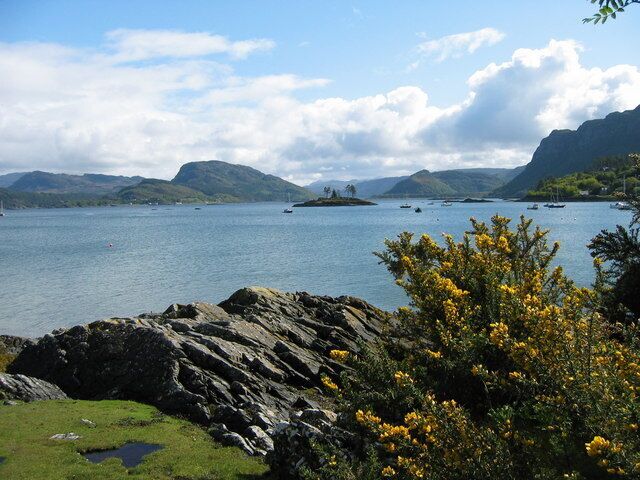 A coastal landscape with rocky shores, a body of water, and distant mountains.