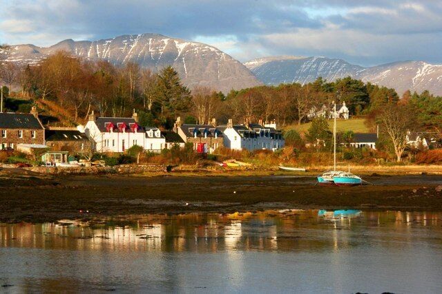 A lakeside village with houses, boats, and mountains in the background.
