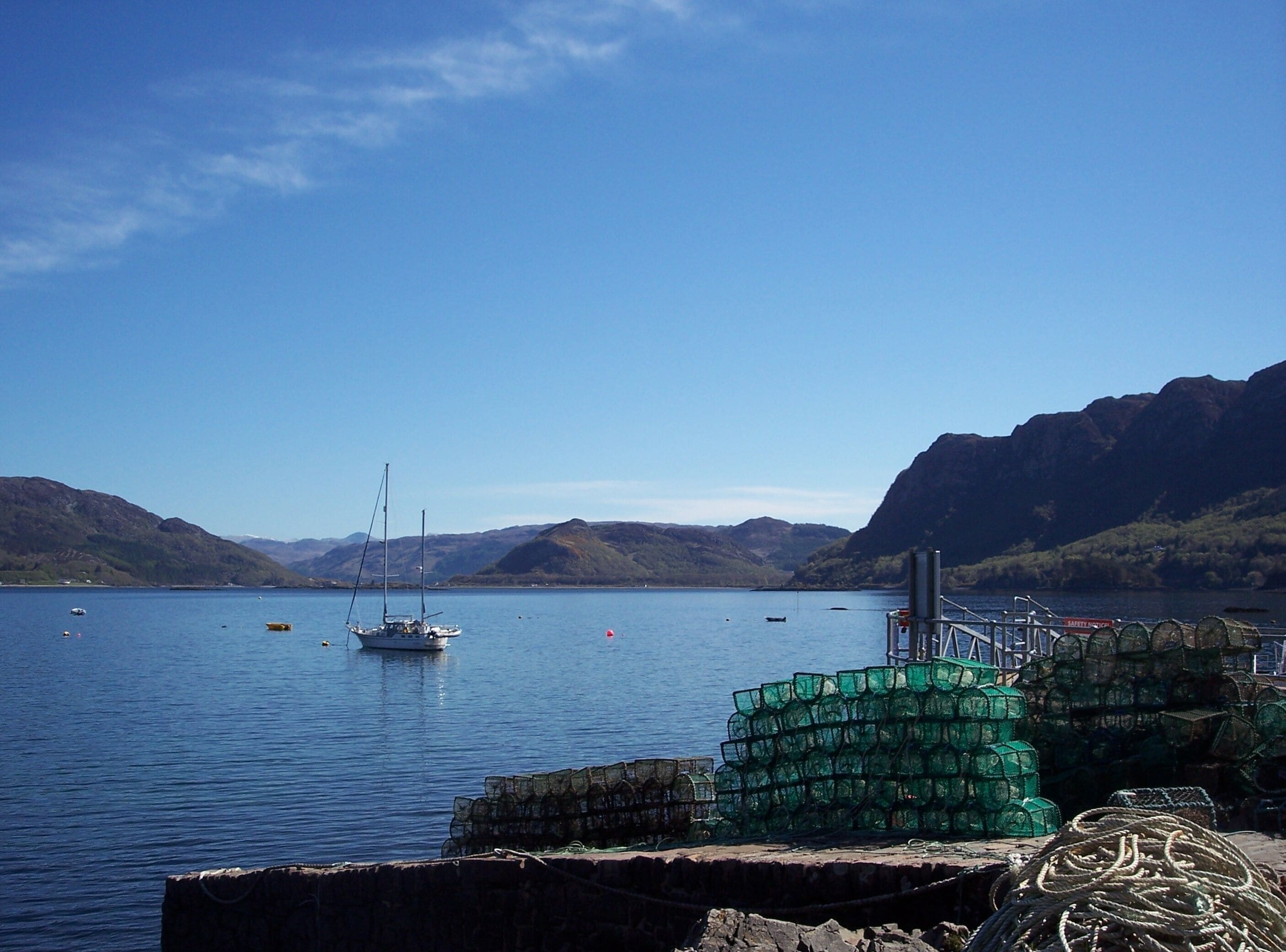 A calm lake with boats, green fishing crates, and mountains in the background.