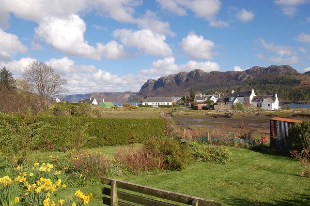 A rural landscape with houses, a lake, and mountains in the background.