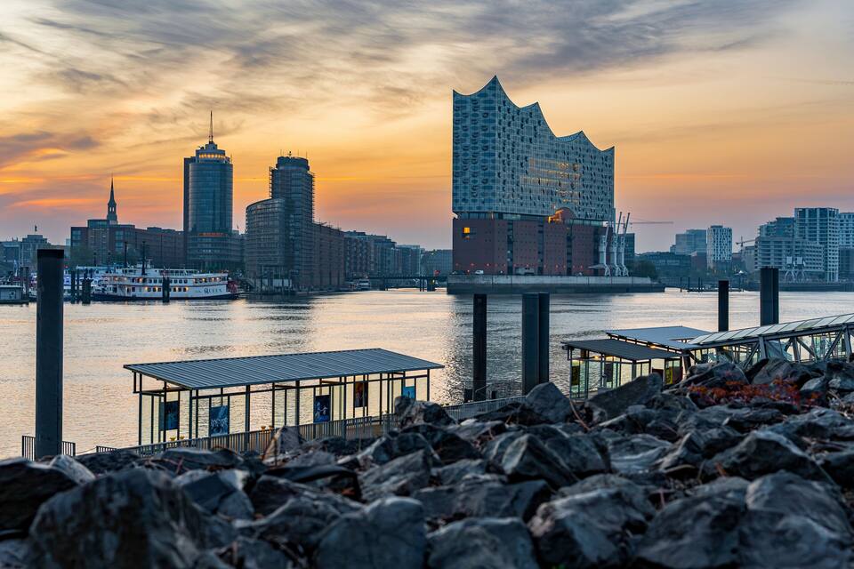 Ein Stadtbild im Abendrot mit einem markanten, modernen Gebäude, einem Fluss und einer Brücke.