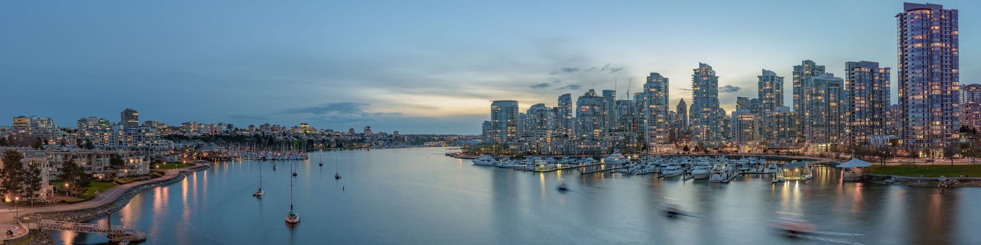 A waterfront cityscape with a marina filled with boats, modern high-rise buildings, and a calm river.