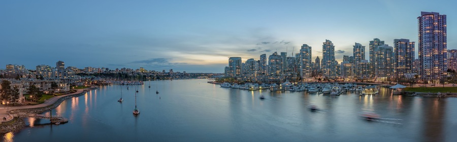 A waterfront cityscape with a marina filled with boats, modern high-rise buildings, and a calm river.