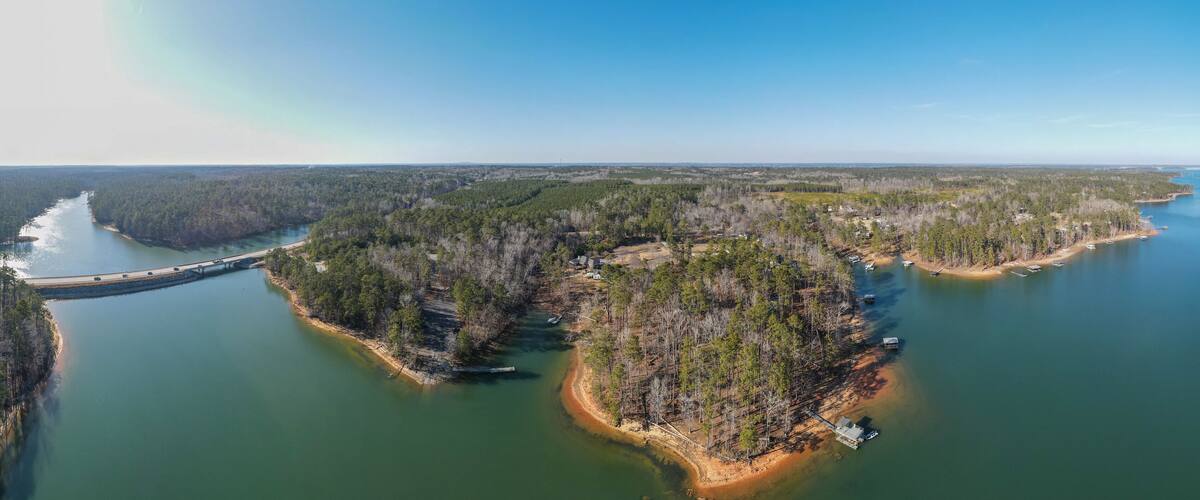 A river winding through a forested landscape with a bridge and several small buildings along the water.