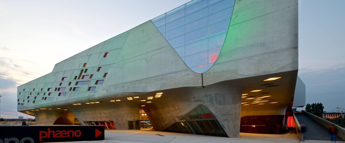 A modern architectural building with a unique angular design, featuring a large glass facade and multiple illuminated windows.