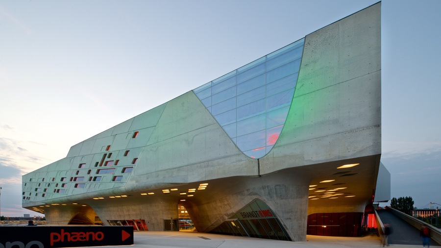 A modern architectural building with a unique angular design, featuring a large glass facade and multiple illuminated windows.