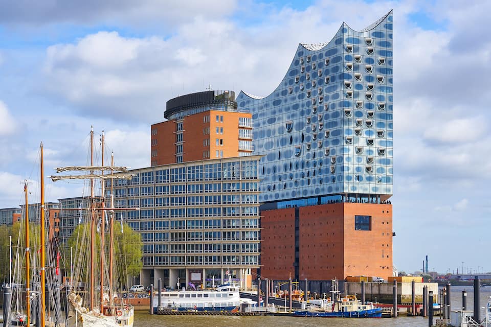En moderne bygning med en buet glasfacade, et traditionelt murstensdomineret tårn og en flod med både.