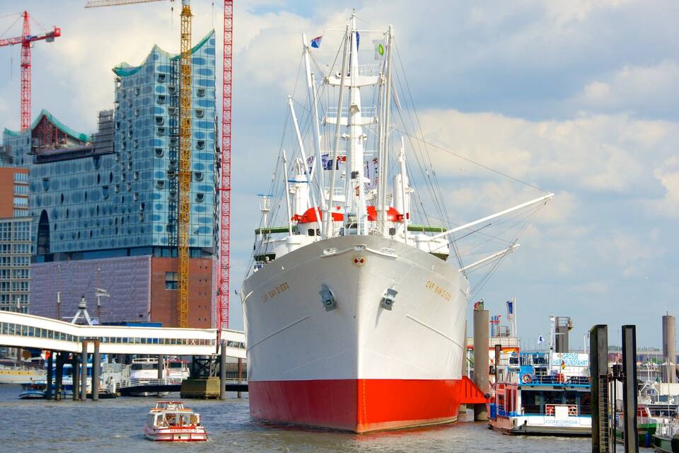 Ein großes Schiff liegt im Hafen vor Anker, mit Kränen und Gebäuden im Hintergrund.