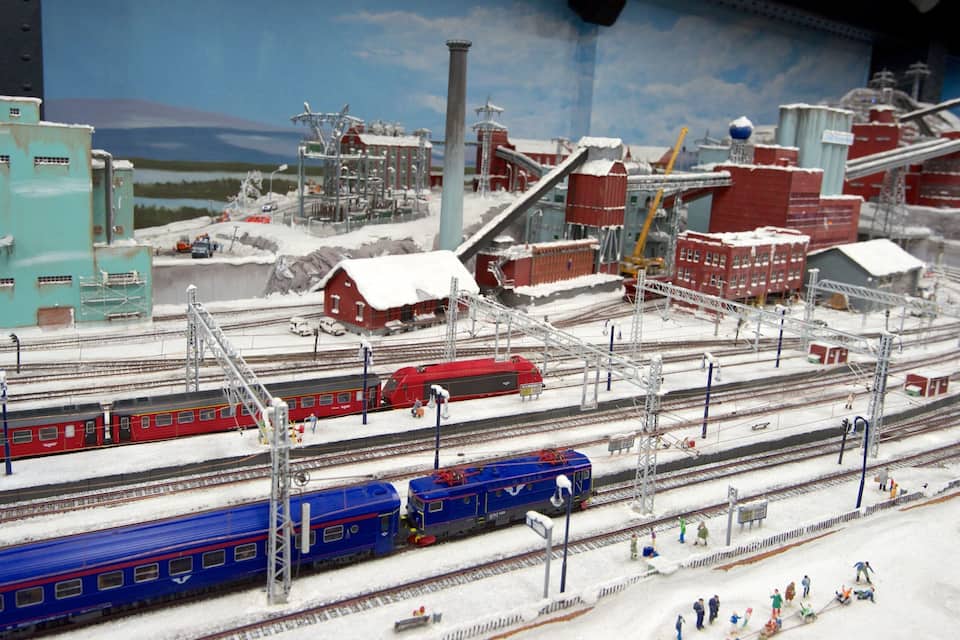 En detaljeret modeljernbane med flere spor, tog og industribygninger.