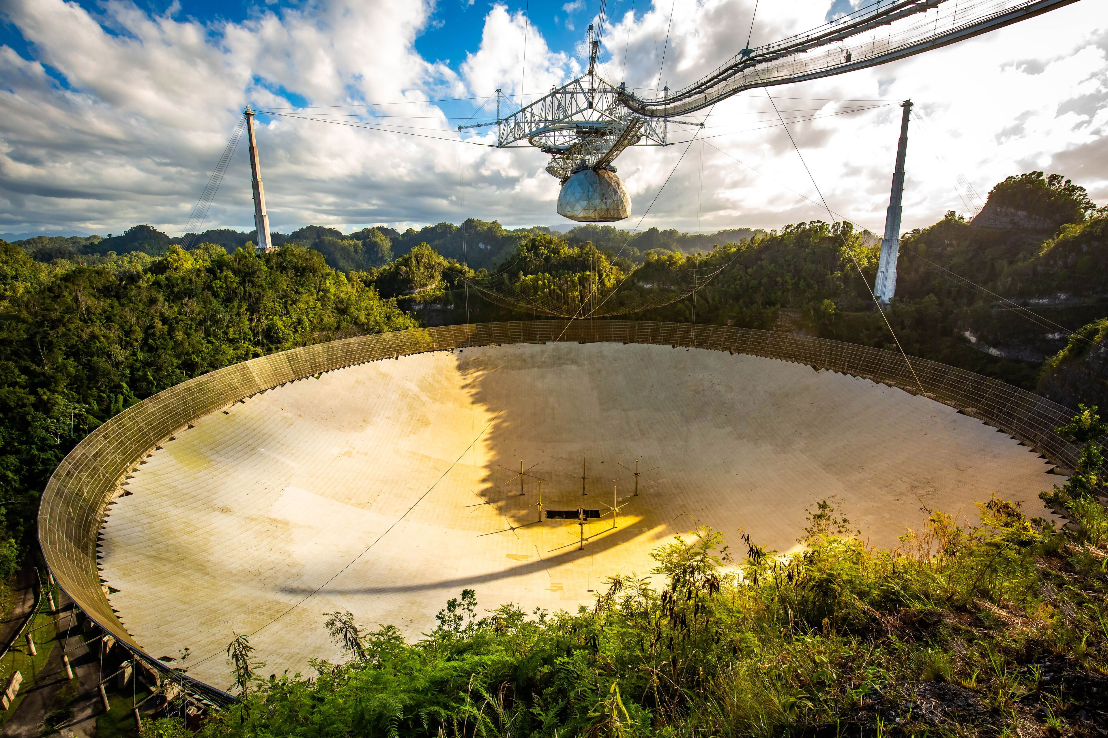 A large, circular structure surrounded by lush greenery and mountains.
