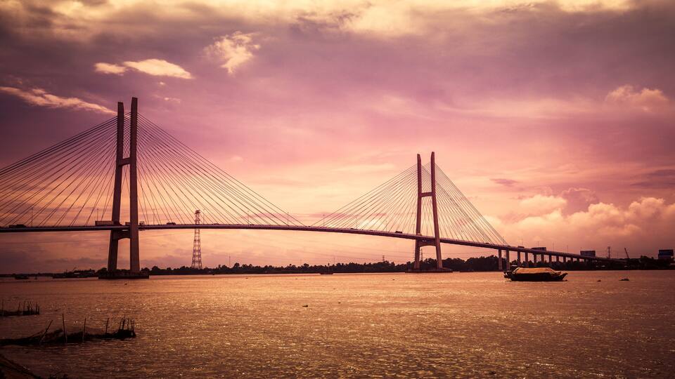 A suspension bridge with cables and towers over a body of water during sunset.