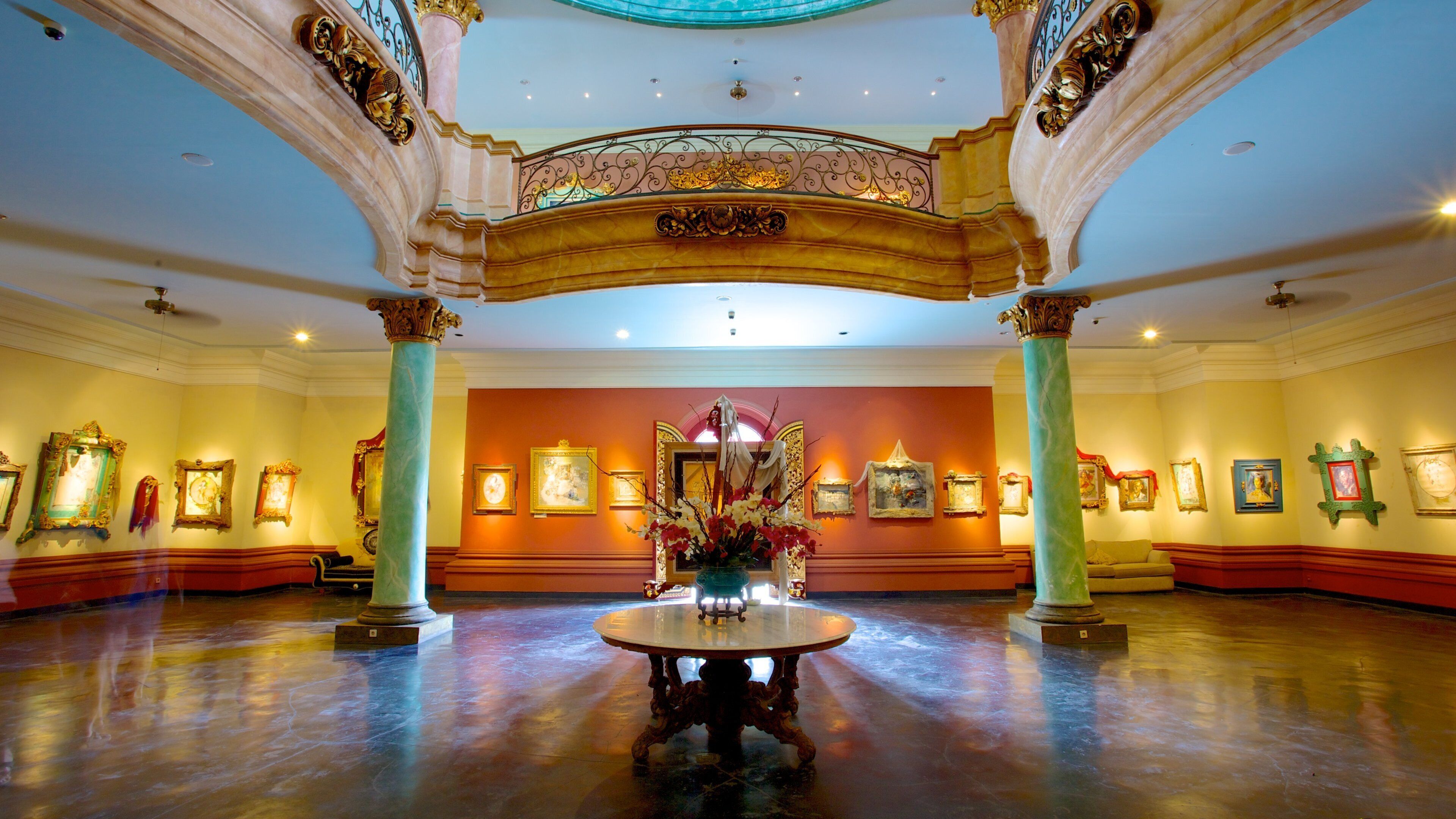 An ornate lobby with a central round table, columns, and framed artwork on the walls.