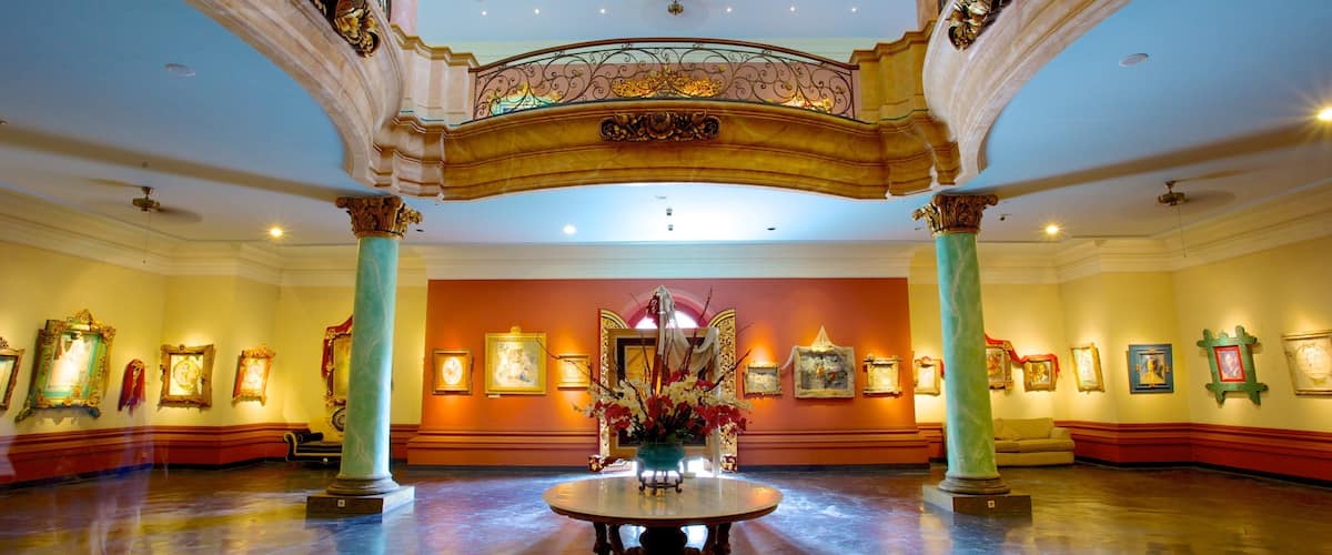An ornate lobby with a central round table, columns, and framed artwork on the walls.