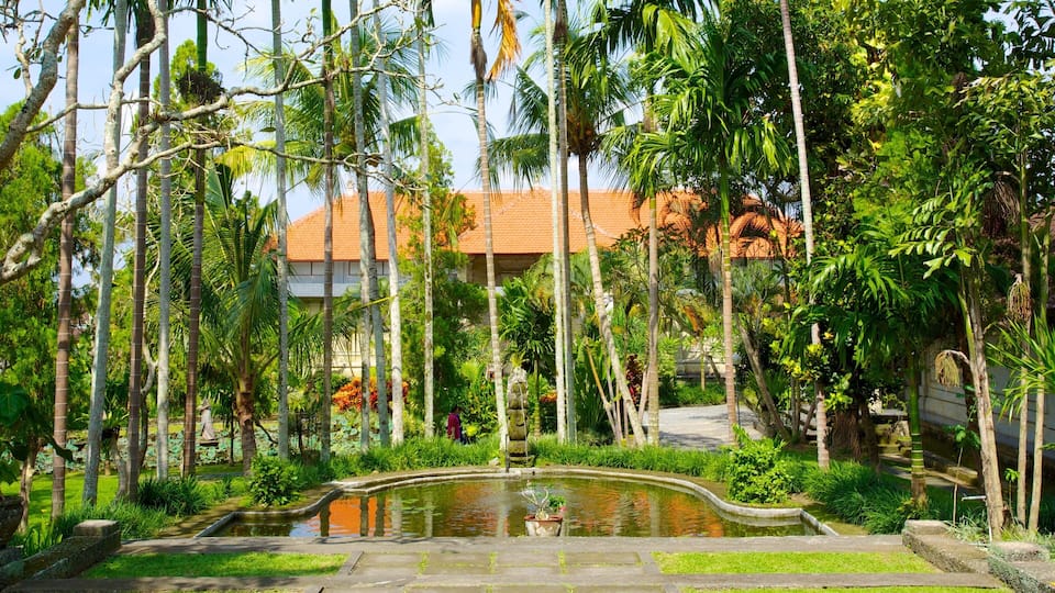 A tropical garden with a pond, palm trees, and a building with a red roof.
