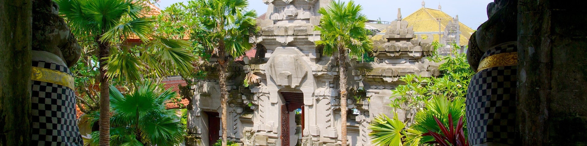 A temple with intricate carvings, surrounded by lush greenery and palm trees.