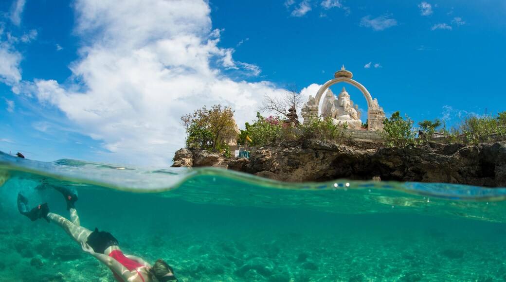 PF8FTK Underwater split-level photo of a female tourist snorkeller & Buddhist temple & statue of Ganesh above, at Menjangan Island, Bali, Indonesia