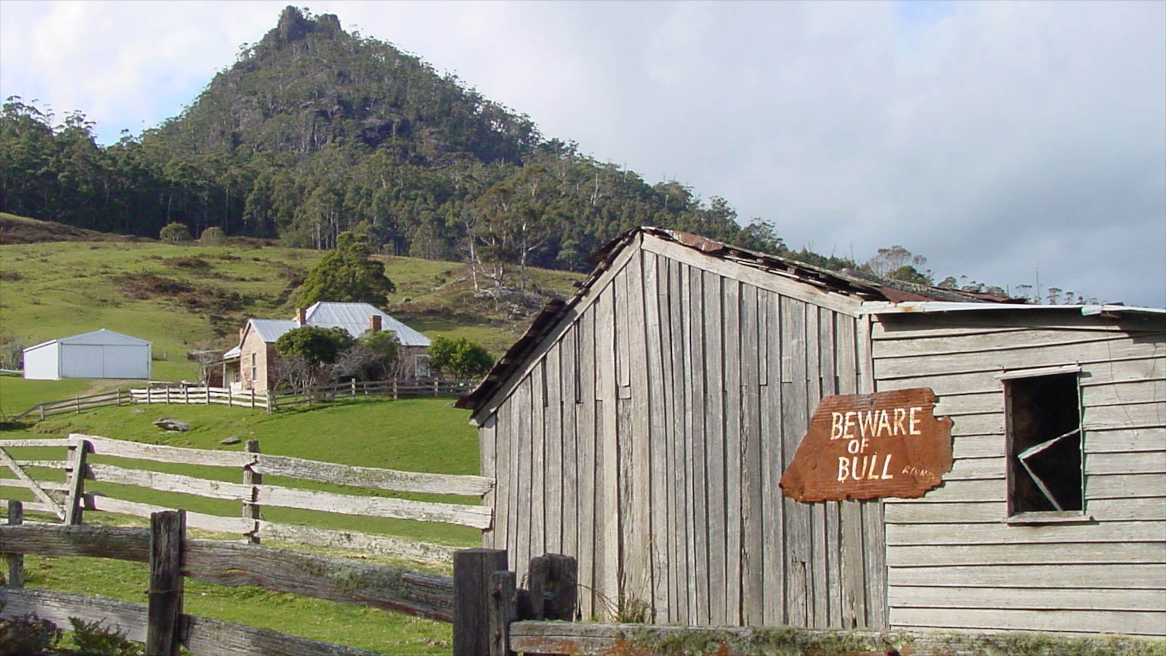 A rural landscape with a wooden barn, a warning sign, and a mountain in the background.